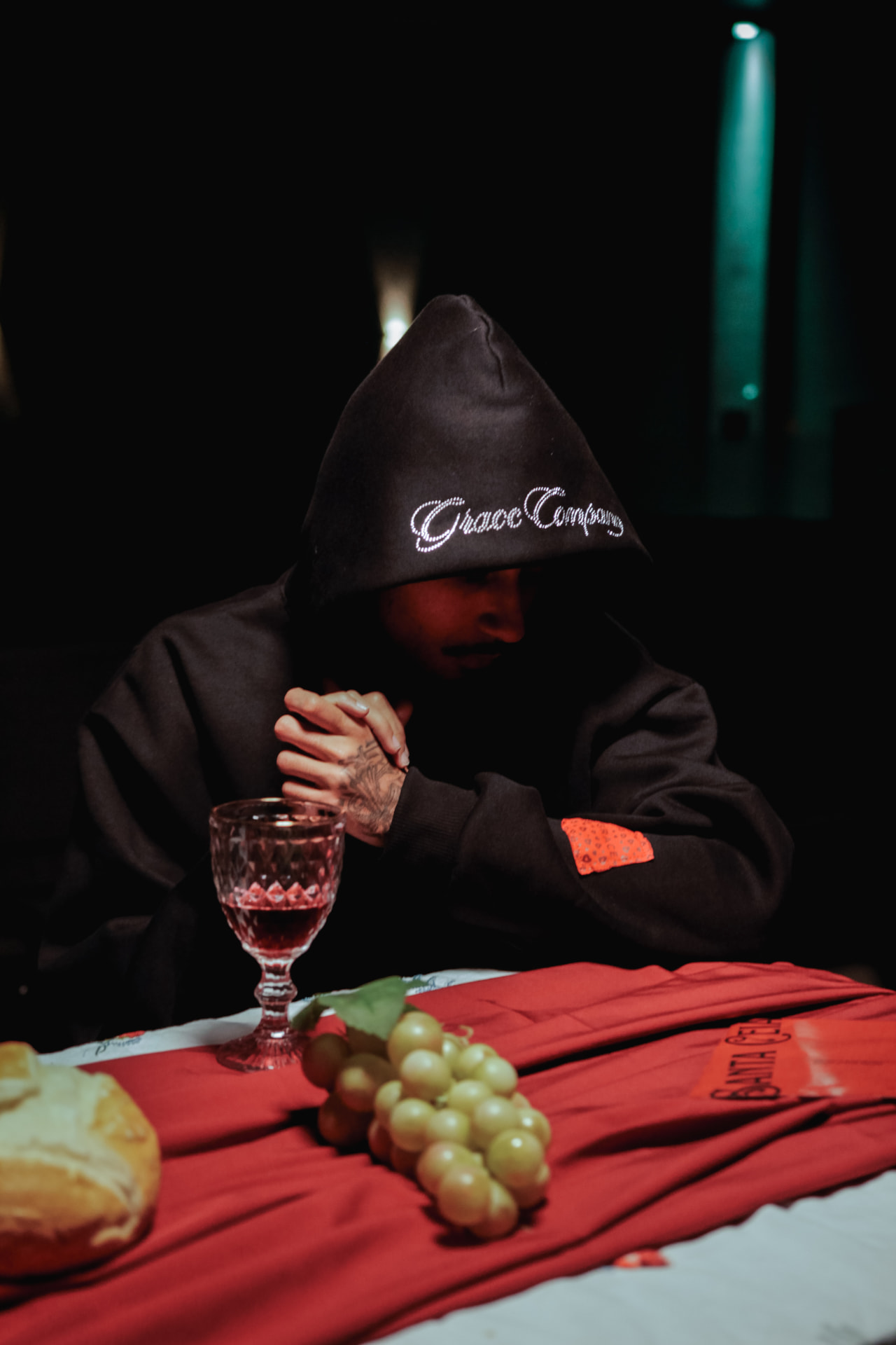 Modelo sentado à mesa com cálice, pão e uvas